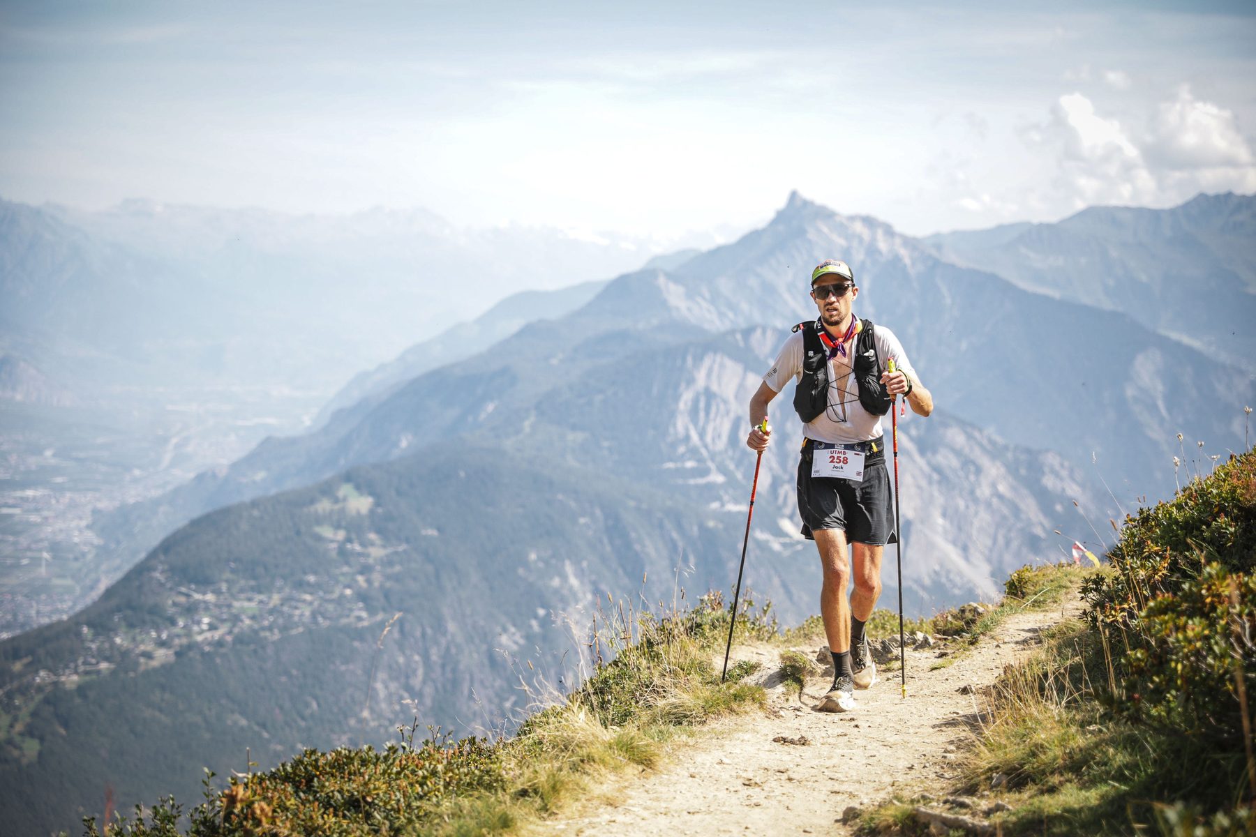 Jack Chamberlain running a high mountain path with poles, a deep valley below.