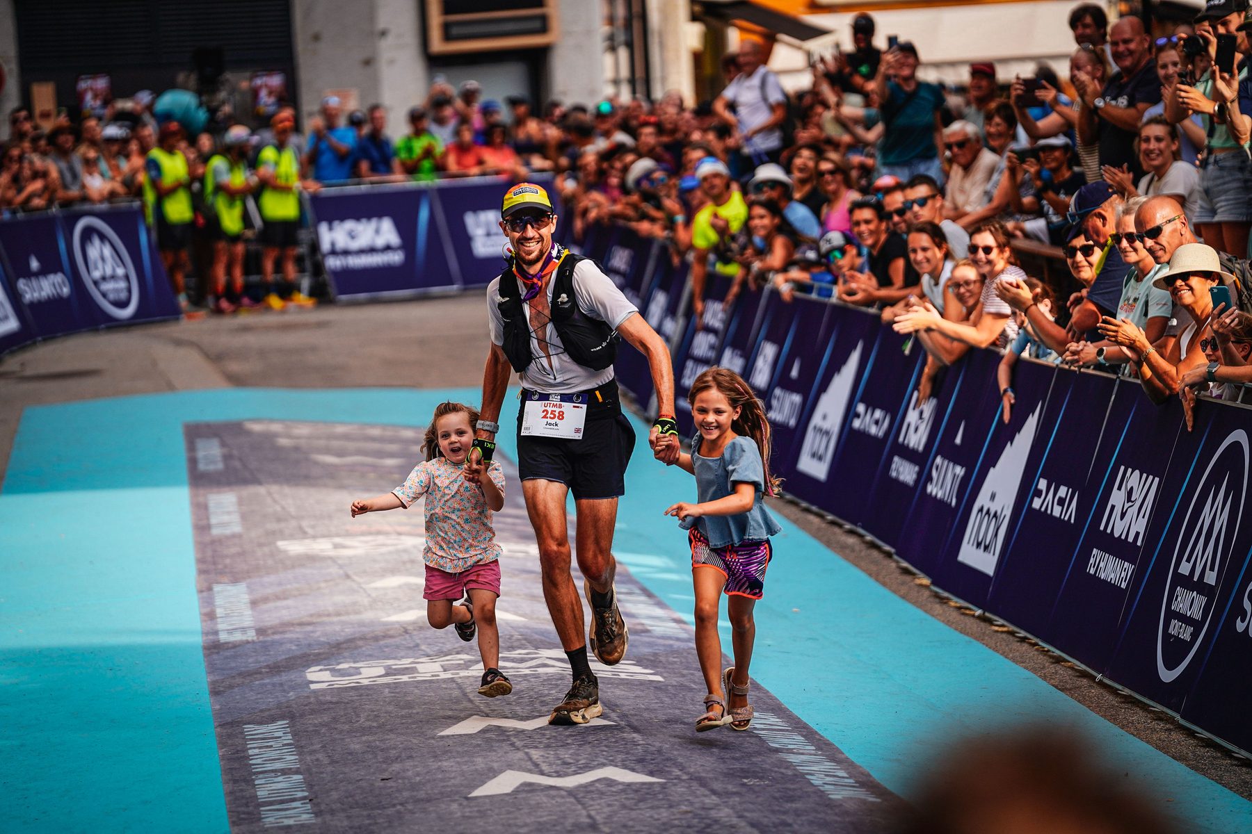 Jack Chamberlain running the UTMB finish chute in Chamonix holding hands with his two daughters.