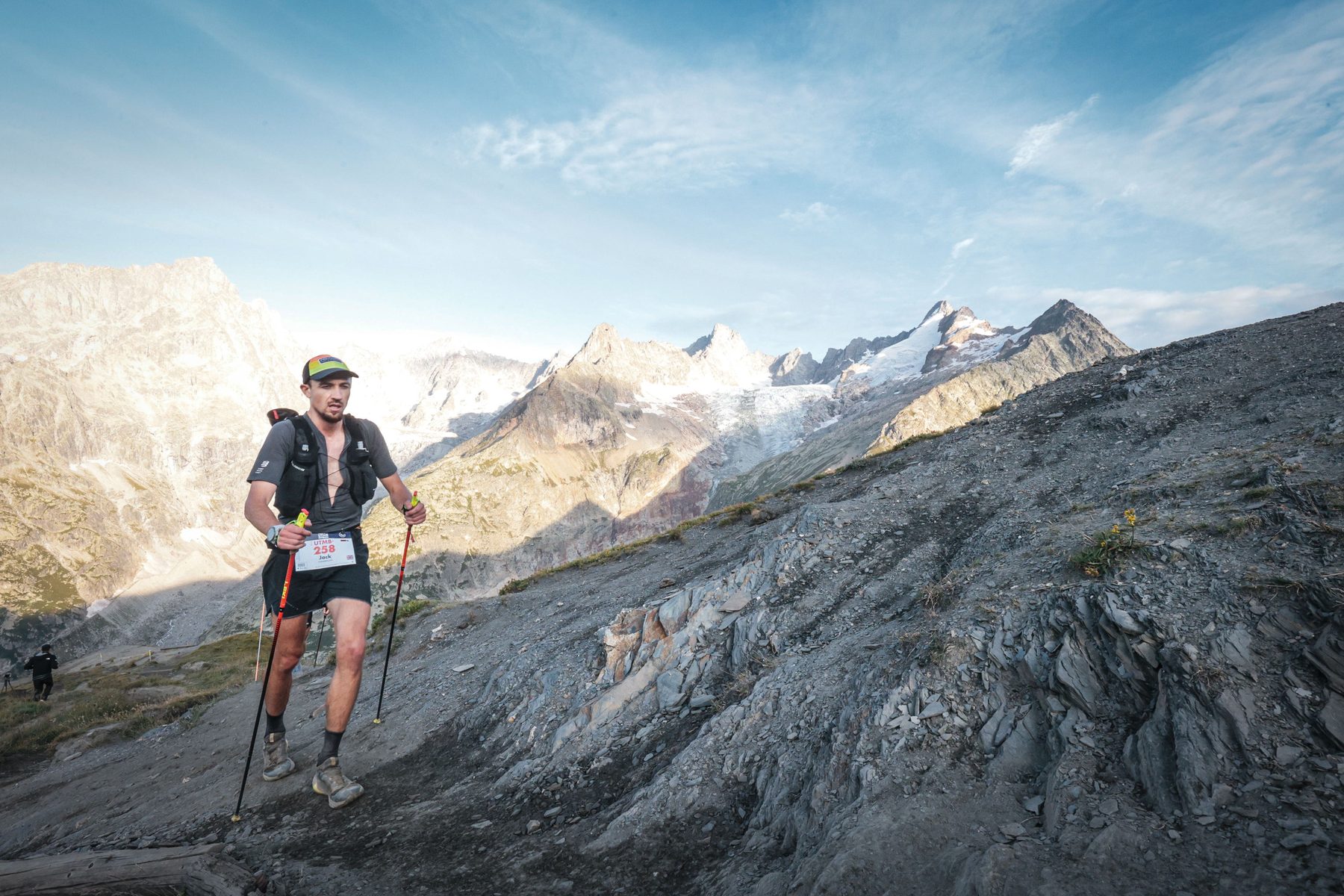 Jack Chamberlain hiking with poles on a rocky alpine traverse above a glacier.
